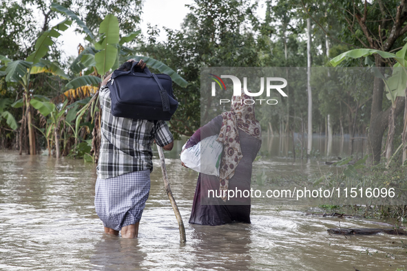 A husband and wife of the same family walk through knee-deep flood water in the Aburhat area of Mirsarai Upazila in Chittagong Division, Ban...