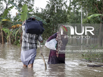 A husband and wife of the same family walk through knee-deep flood water in the Aburhat area of Mirsarai Upazila in Chittagong Division, Ban...