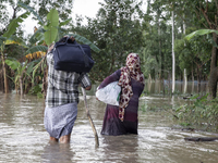 A husband and wife of the same family walk through knee-deep flood water in the Aburhat area of Mirsarai Upazila in Chittagong Division, Ban...