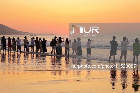 Tourists watch the sunrise at the Golden Beach in Qingdao, China, on August 28, 2024. 