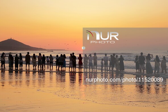 Tourists watch the sunrise at the Golden Beach in Qingdao, China, on August 28, 2024. 