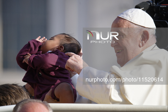 Pope Francis caresses a newborn as he arrives for his weekly General Audience in Saint Peter's Square, Vatican City, on August 28, 2024. 