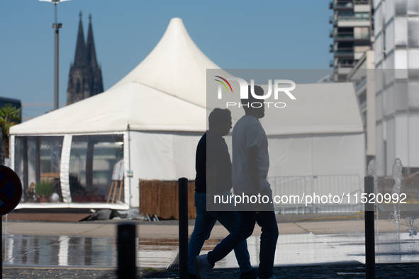 People walk at Harry Blum Square as Cologne Cathedral is seen in the background in Cologne, Germany, on August 28, 2024. 