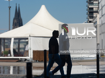 People walk at Harry Blum Square as Cologne Cathedral is seen in the background in Cologne, Germany, on August 28, 2024. (