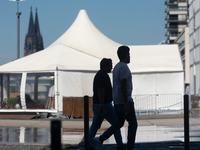 People walk at Harry Blum Square as Cologne Cathedral is seen in the background in Cologne, Germany, on August 28, 2024. (