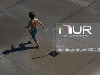 A boy plays with water from a fountain at Harry Blum Square in Cologne, Germany, on August 28, 2024. (