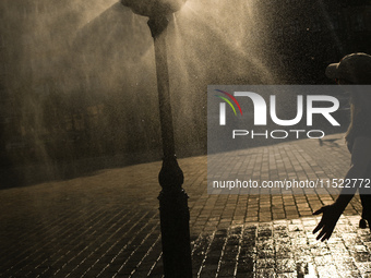 KRAKOW, POLAND - AUGUST 28:
A person cools down under the water sprinkler set up in Podgorze's Market Square as Southern Poland and Krakow e...