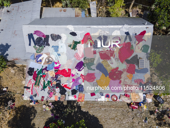 A flood-affected family dries clothes and essential items soaked in flood water on the roof of a house in Gopal village of Chagalnaiya upazi...