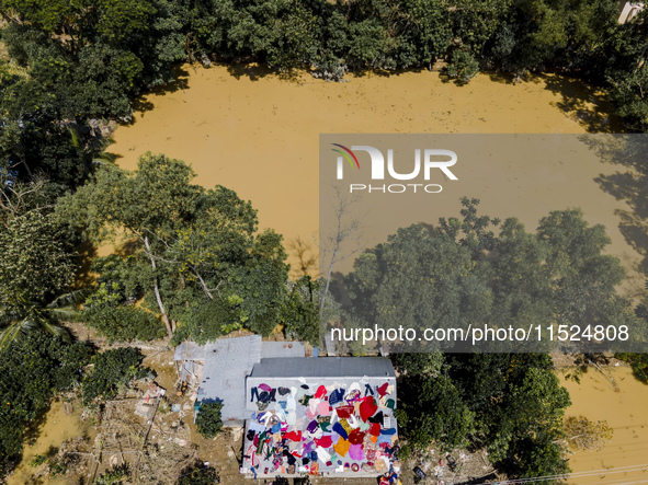 A flood-affected family dries clothes and essential items soaked in flood water on the roof of a house in Gopal village of Chagalnaiya upazi...