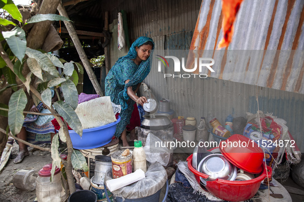 A member of a flood-affected family cooks lunch outside the house among the messy belongings in Gopal area of Chagalnaia upazila in Feni dis...