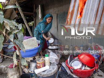 A member of a flood-affected family cooks lunch outside the house among the messy belongings in Gopal area of Chagalnaia upazila in Feni dis...