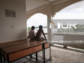 Two small boys sit on a table on the balcony of a shelter watching the flooding outside in Chagalnaiya Upazila, Feni District, Chittagong Di...