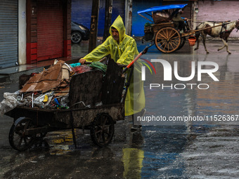 An employee of the municipality sweeps and puts garbage in a cart on a rainy day in Sopore, Jammu and Kashmir, India, on August 30, 2024. (