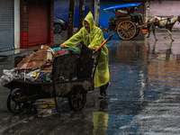 An employee of the municipality sweeps and puts garbage in a cart on a rainy day in Sopore, Jammu and Kashmir, India, on August 30, 2024. (