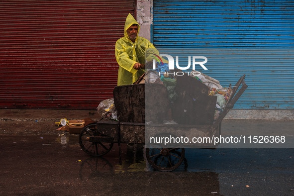 An employee of the municipality sweeps and puts garbage in a cart on a rainy day in Sopore, Jammu and Kashmir, India, on August 30, 2024. 