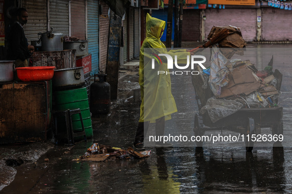 An employee of the municipality sweeps and puts garbage in a cart on a rainy day in Sopore, Jammu and Kashmir, India, on August 30, 2024. 