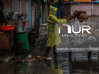 An employee of the municipality sweeps and puts garbage in a cart on a rainy day in Sopore, Jammu and Kashmir, India, on August 30, 2024. (