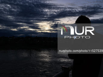 A young boy shoots video as clouds hover above during an evening in Sopore, Jammu and Kashmir, India, on August 30, 2024. (