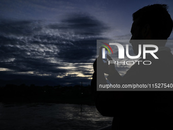 A young boy shoots video as clouds hover above during an evening in Sopore, Jammu and Kashmir, India, on August 30, 2024. (