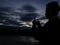 A young boy shoots video as clouds hover above during an evening in Sopore, Jammu and Kashmir, India, on August 30, 2024. (