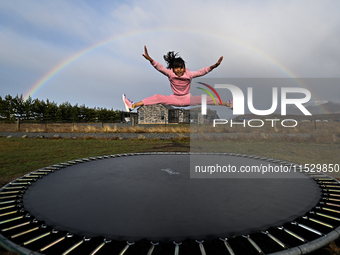 A little girl, Minudi Menulya, jumps on a trampoline as a rainbow glows in the background in Twizel, New Zealand, on August 31, 2024. (