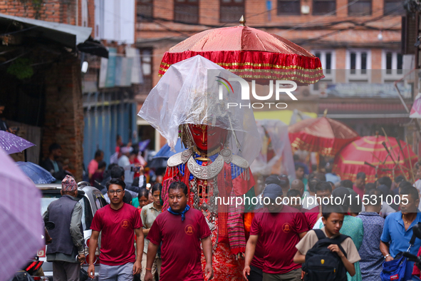 Nepali devotees carry the statues of Dipankar Buddha, covering them with plastic sheets as it rains heavily during the Panchadan festival in...