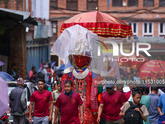 Nepali devotees carry the statues of Dipankar Buddha, covering them with plastic sheets as it rains heavily during the Panchadan festival in...