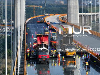 Workers spread asphalt on the deck of the main bridge of the Longtan Yangtze River Bridge in Yangzhou, China, on September 1, 2024. (