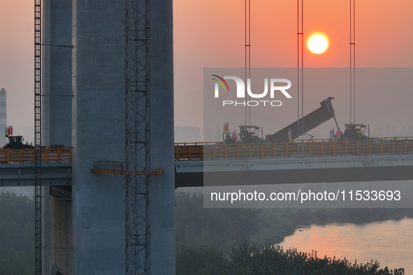 Workers spread asphalt on the deck of the main bridge of the Longtan Yangtze River Bridge in Yangzhou, China, on September 1, 2024. 