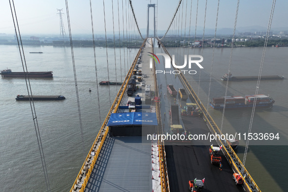 Workers spread asphalt on the deck of the main bridge of the Longtan Yangtze River Bridge in Yangzhou, China, on September 1, 2024. 