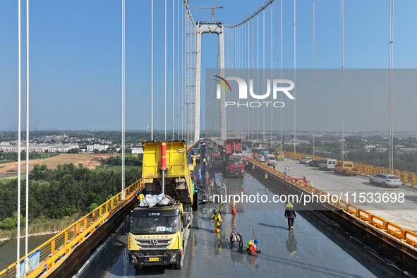 Workers spread asphalt on the deck of the main bridge of the Longtan Yangtze River Bridge in Yangzhou, China, on September 1, 2024. 