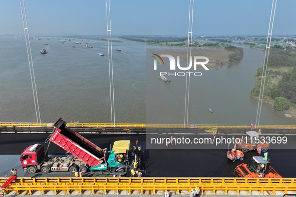 Workers spread asphalt on the deck of the main bridge of the Longtan Yangtze River Bridge in Yangzhou, China, on September 1, 2024. 