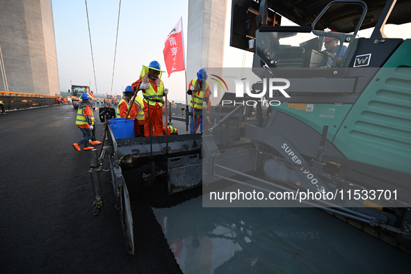 Workers spread asphalt on the deck of the main bridge of the Longtan Yangtze River Bridge in Yangzhou, China, on September 1, 2024. 