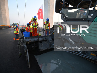 Workers spread asphalt on the deck of the main bridge of the Longtan Yangtze River Bridge in Yangzhou, China, on September 1, 2024. (