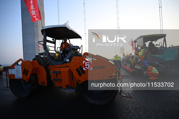 Workers spread asphalt on the deck of the main bridge of the Longtan Yangtze River Bridge in Yangzhou, China, on September 1, 2024. 