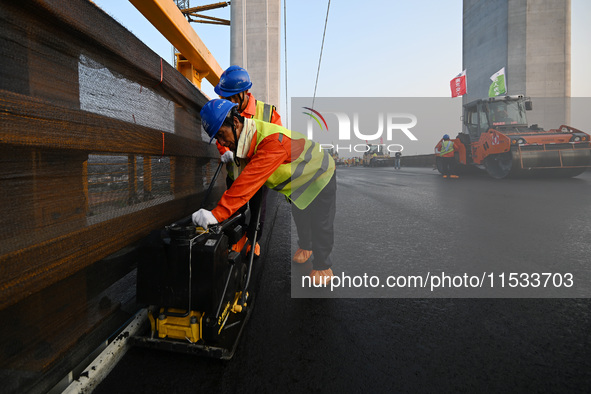 Workers spread asphalt on the deck of the main bridge of the Longtan Yangtze River Bridge in Yangzhou, China, on September 1, 2024. 