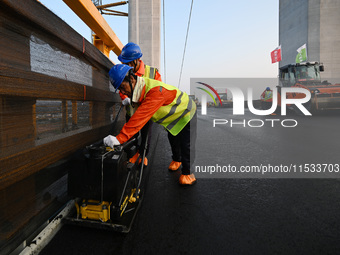 Workers spread asphalt on the deck of the main bridge of the Longtan Yangtze River Bridge in Yangzhou, China, on September 1, 2024. (