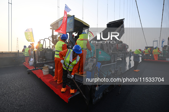 Workers spread asphalt on the deck of the main bridge of the Longtan Yangtze River Bridge in Yangzhou, China, on September 1, 2024. 