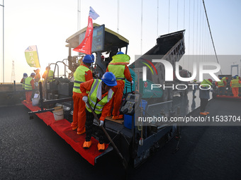 Workers spread asphalt on the deck of the main bridge of the Longtan Yangtze River Bridge in Yangzhou, China, on September 1, 2024. (