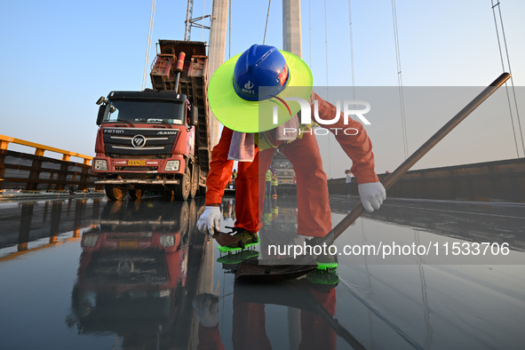 Workers spread asphalt on the deck of the main bridge of the Longtan Yangtze River Bridge in Yangzhou, China, on September 1, 2024. 