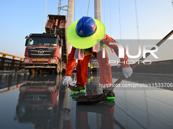 Workers spread asphalt on the deck of the main bridge of the Longtan Yangtze River Bridge in Yangzhou, China, on September 1, 2024. (