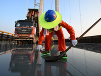 Workers spread asphalt on the deck of the main bridge of the Longtan Yangtze River Bridge in Yangzhou, China, on September 1, 2024. (