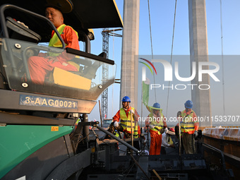 Workers spread asphalt on the deck of the main bridge of the Longtan Yangtze River Bridge in Yangzhou, China, on September 1, 2024. (