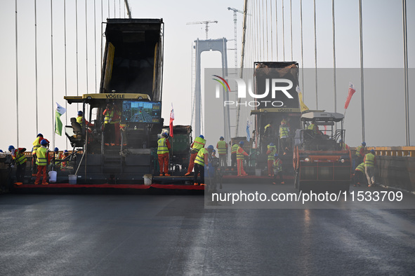 Workers spread asphalt on the deck of the main bridge of the Longtan Yangtze River Bridge in Yangzhou, China, on September 1, 2024. 