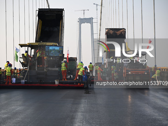 Workers spread asphalt on the deck of the main bridge of the Longtan Yangtze River Bridge in Yangzhou, China, on September 1, 2024. (