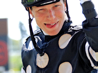 Jockey Emma-Jayne Wilson gestures to a video broadcast camera as she rides Ask in My Name to the winner's circle after a win in the second r...