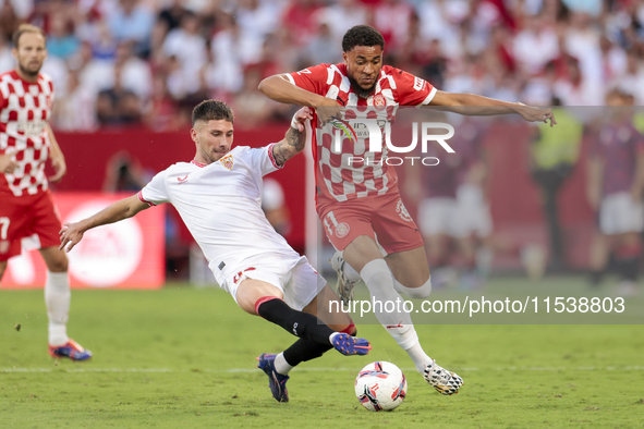 Arnau Danjuma of Girona FC competes for the ball with Jose Angel Carmona of Sevilla FC during the La Liga EA Sports match between Sevilla FC...