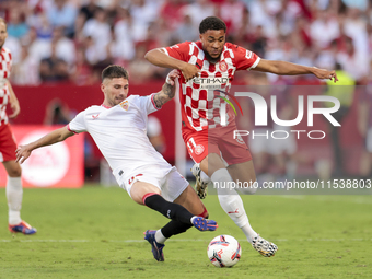 Arnau Danjuma of Girona FC competes for the ball with Jose Angel Carmona of Sevilla FC during the La Liga EA Sports match between Sevilla FC...