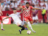 Arnau Danjuma of Girona FC competes for the ball with Jose Angel Carmona of Sevilla FC during the La Liga EA Sports match between Sevilla FC...