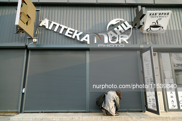 A woman lifts a security shutter at a pharmacy in the Sviatoshynskyi district after the Russian missile attack in Kyiv, Ukraine, on Septembe...